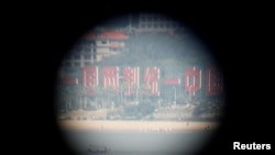 FILE - China's banner reading "One Country, Two Systems, One Unified China" is seen through a tourist's binoculars from a former military fort, ahead of the 60th anniversary of Second Taiwan Straits Crisis against China, in Lieyu island, Kinmen county, Taiwan, Aug. 20, 2018.