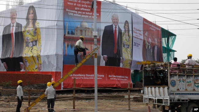 Un trabajador pinta un poste junto a una valla publicitaria con la fotografía del presidente de Estados Unidos, Donald Trump, y la primera dama Melania Trump, erigida para recibirlos en Agra, India, el domingo 23 de febrero de 2020.