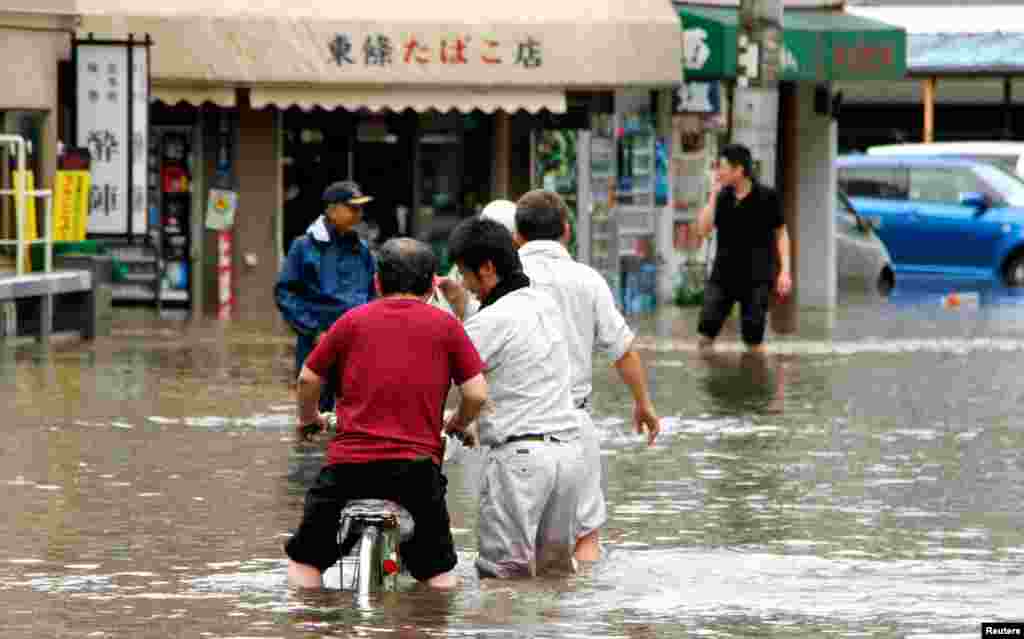 People wade through a flooded street caused by heavy rains in Kumamoto, southwestern Japan.