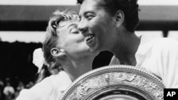 Althea Gibson holds the Wimbledon women's singles trophy as she gets a kiss from Darlene Hard, whom she defeated at Wimbledon in England in this July 6, 1957 file photo. 