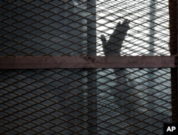 FILE - A defendant is seen caged in a courtroom in Torah prison, southern Cairo, Egypt, Aug. 22, 2015.