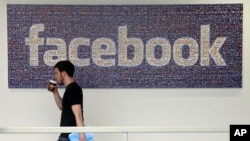  In this March 15, 2013, photo, a Facebook employee walks past a sign at Facebook headquarters in Menlo Park, Calif.