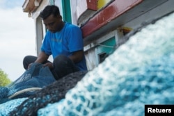 Seorang nelayan memegang jaring ikan di perahu kayunya di Aceh, 29 Desember 2021. (Foto : Reuters)