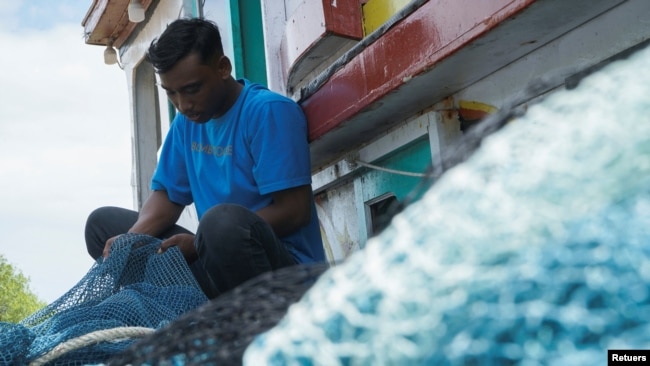 Local fisherman Aditya Setiawan, 20, holds a fishing net at his wooden boat during an interview as a witness, following a boat carrying Rohingya refugees being stranded at sea off the coast of Bireuen, Aceh province, Indonesia, December 29, 2021. (REUTERS