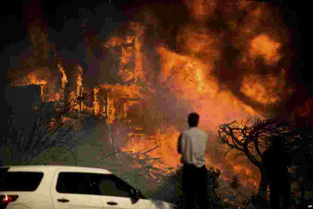A man watches flames consume a residence as a wildfire rages in Ventura, Dec. 5, 2017.