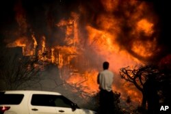 A man watches flames consume a residence as a wildfire rages in Ventura, Calif., Dec. 5, 2017.