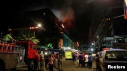 Evacuated employees and guests of the hotel stand along a road and watch as smoke billows from a Resorts World building in Pasay City, Manila, Philippines, June 2, 2017.