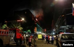 Evacuated employees and guests of hotels stand along a road and watch as smoke billows from a Resorts World building in Pasay City, Metro Manila, Philippines, June 2, 2017.