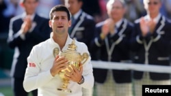 Novak Djokovic of Serbia reacts while holding the winner's trophy after defeating Roger Federer of Switzerland in their men's singles finals tennis match on Centre Court at the Wimbledon Tennis Championships in London July 6, 2014. 