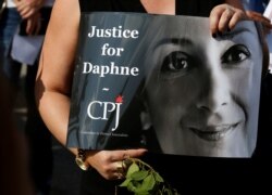 FILE - A person holds a placard depicting Daphne Caruana Galizia, prepared by Committee to Protect Journalists (CPJ), as people gather at the site where the journalist was assassinated in a car bomb one year ago, in Bidnija, Malta, Oct. 16, 2018.