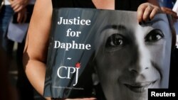 A person holds a placard depicting Daphne Caruana Galizia, prepared by Committee to Protect Journalists (CPJ), as people gather at the site where anti-corruption journalist was assassinated in a car bomb one year ago, in Bidnija, Malta, Oct. 16, 2018.