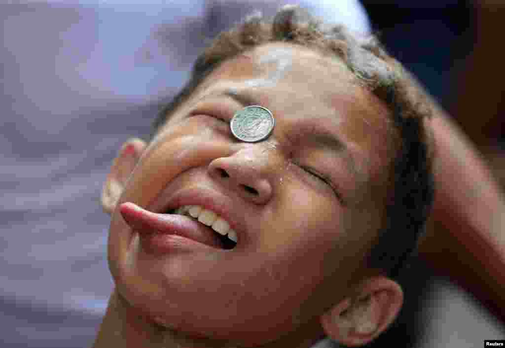 A boy attempts to move a coin into his mouth during a celebration of the patron saint Santa Rita de Cascia in Baclaran, Paranaque city, metro Manila, Philippines.