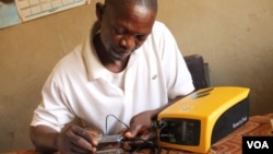 Michael Mugerwa uses his solar system to charge phones in Kiwumu, Uganda, Feb. 28, 2014. (Hilary Heuler/VOA)