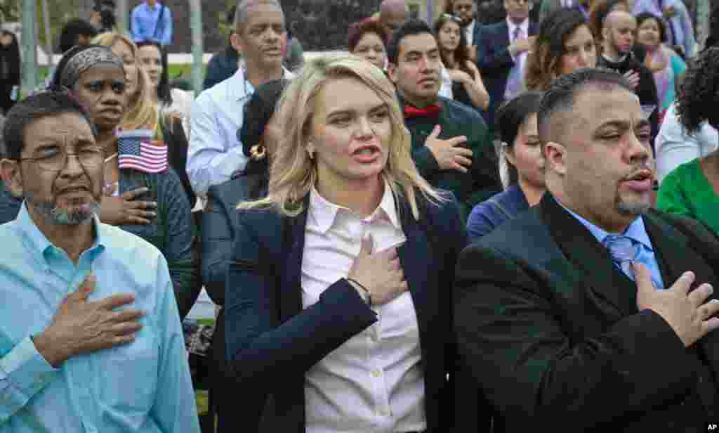 Immigrants from 24 countries, raise their hands to their chest as the National Anthem played during a U.S. Citizen and Immigration Services (USCIS) naturalization ceremony, in New York.