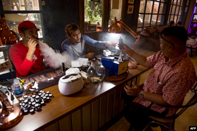 Seorang karyawan kafe rokok elektrik (kiri) melayani pembeli di Jakarta. (Foto: AFP)