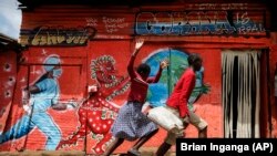 Children run down a street past an informational mural warning people about the dangers of coronavirus in the Kibera slum of Nairobi, Kenya on Wednesday, June 3, 2020.
