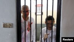 FILE - Canadian teacher Neil Bantleman (L) waves beside Indonesian teaching assistant Ferdinand Tjiong to students as they wait inside a holding cell before their trial at a South Jakarta court, Indonesia, April 2, 2015. 