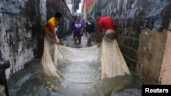 FILE - Men use a mosquito net to catch fish in a flooded alley in a residential district in Bacoor, near Manila, Phillippines, Aug. 20, 2013.