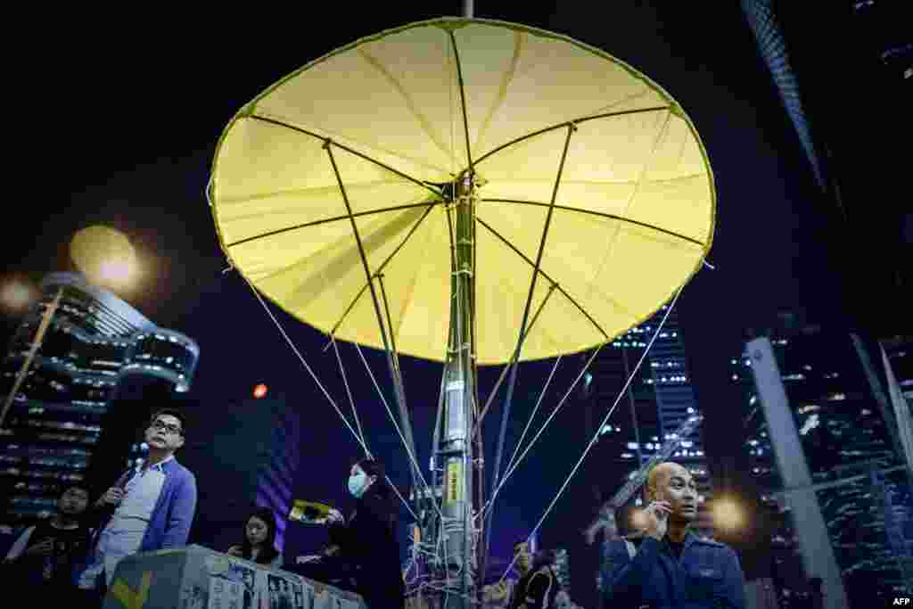 People walk under a lamp post turned into a yellow umbrella near the main stage of the protest site of the Admiralty district of Hong Kong. Pro-democracy protesters are at a crossroads as public support fades after nearly two months of slowed traffic and street demostrations.