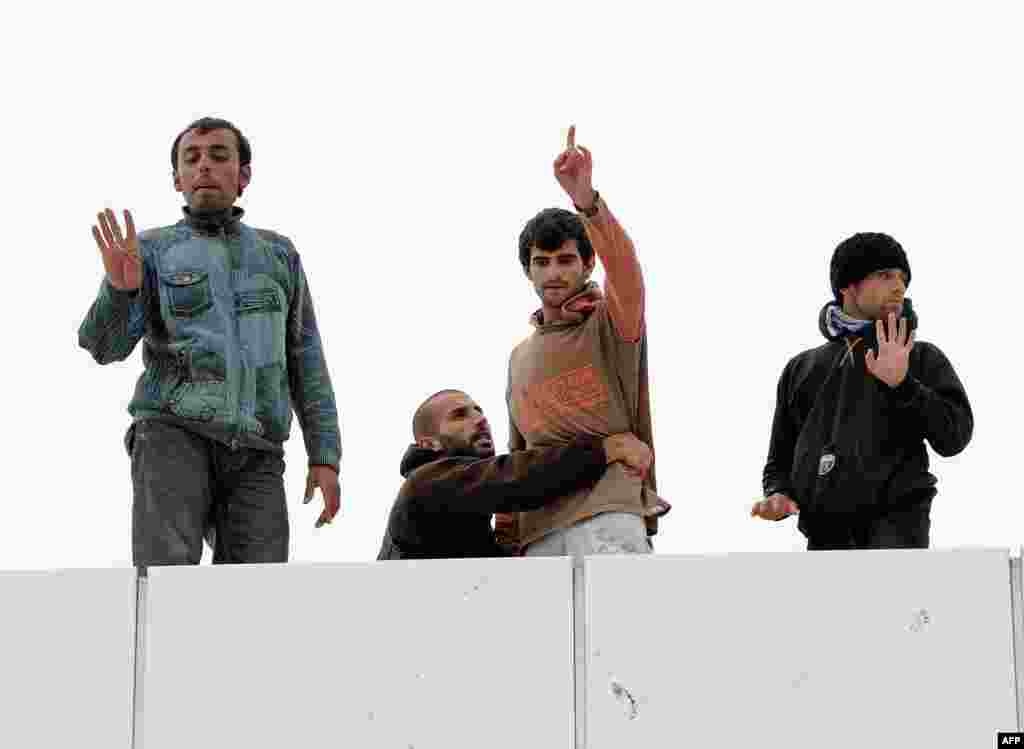 A Syrian refugee prevents another one from jumping from the top of a building as they protest at the ferry terminal in Calais, northern France. A team of British border police began talks with Syrian refugees, some on hunger strike, who are blocking a gangway at a ferry terminal in Calais in a desperate bid to win asylum in Britain.