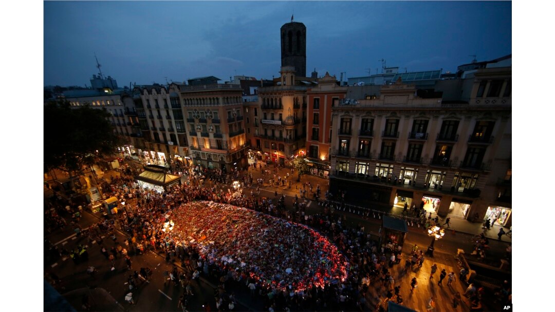 People stand around a memorial tribute of flowers, messages and candles on Barcelona's historic Las Ramblas promenade as night falls following a demonstration condemning the attacks that killed 15 people last week in Barcelona, Spain, Aug. 26, 2017.