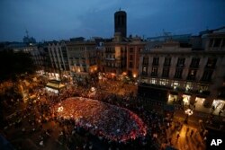 People stand around a memorial tribute of flowers, messages and candles on Barcelona's historic Las Ramblas promenade as night falls following a demonstration condemning the attacks that killed 15 people last week in Barcelona, Spain, Aug. 26, 2017.