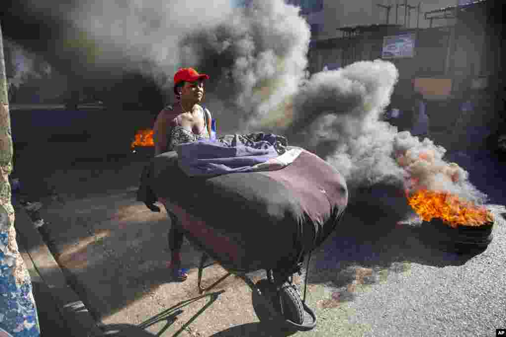 A woman pushes her merchandize away from tires set fire by protesters during a countrywide strike demanding the resignation of Haitian President Jovenel Moise in Port-au-Prince.