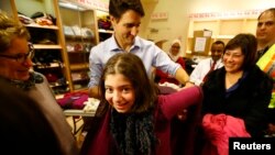 Canada's Prime Minister Justin Trudeau helps a young Syrian refugee try on a winter coat after she arrived with her family from Beirut at the Toronto Pearson International Airport in Mississauga, Ontario, Canada December 11, 2015. (REUTERS/Mark Blinch)