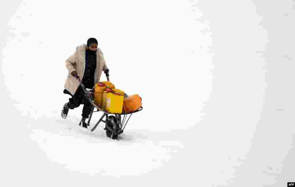 A man pushes a wheelbarrow carrying water cans as snow falls in Kabul, Afghanistan.