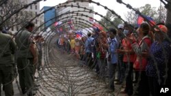 Cambodian garment workers, right, are blocked by barbed wire set up by police near the Council of Ministers building during a rally in Phnom Penh, Cambodia, Monday, Dec. 30, 2013. The workers are demanding a raise in their monthly salary from US $160 to $80. (AP Photo/Heng Sinith)