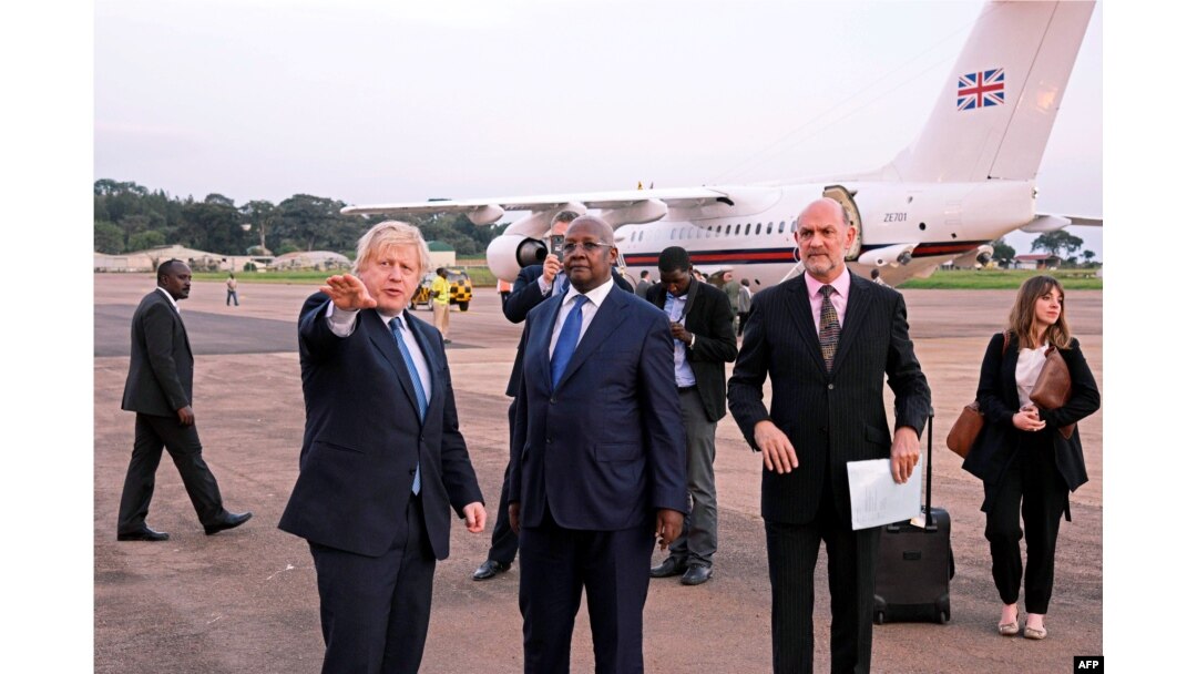 Ministar spoljnih poslova Ugande Sem Kahamba Kutesa (u sredini) ukazuje dobrodošlicu ministru spoljnih poslova Velike Britanije, Borisu Džonsonu (levo) uz britanskog visokog predstavnika za Ugandu Piterom Vestom (desno), nakon njihovog sletanja na Entebe međunarodni aerodrom 15. marta 2017.
