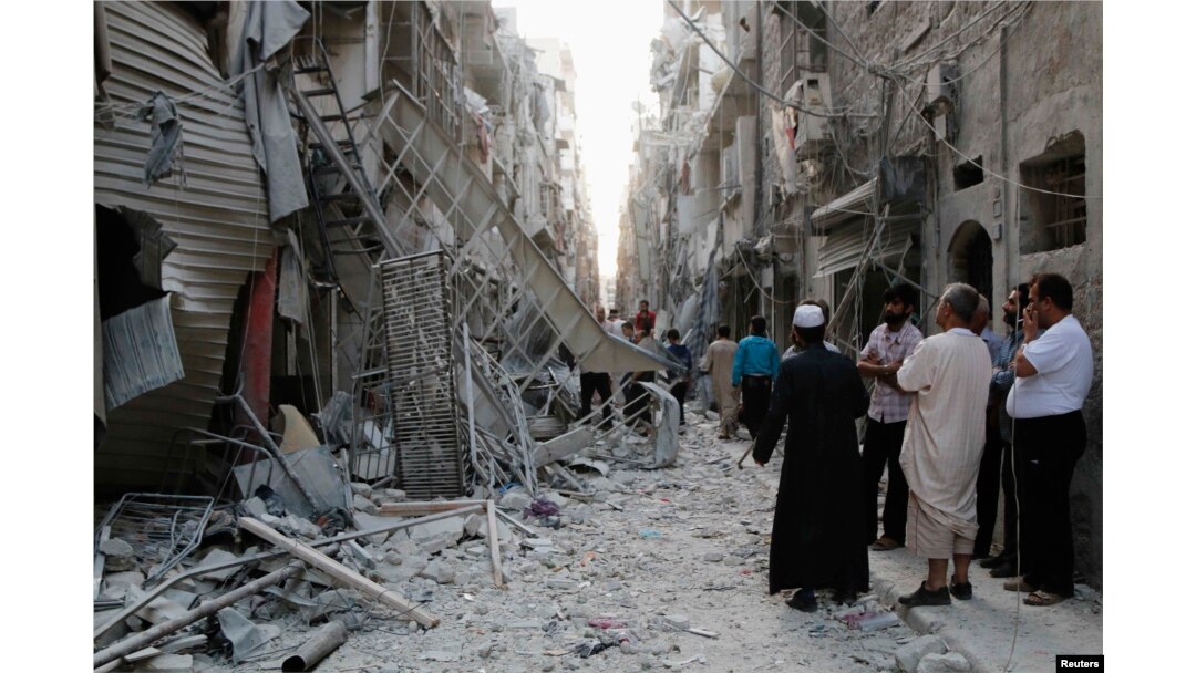 FILE - People stand near damaged buildings along a street at a site hit by what activists said was a barrel bomb dropped by forces loyal to Syria's President Bashar al-Assad in Aleppo's Bustan al-Qasr neighborhood May 28, 2014.