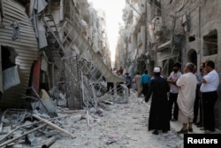 FILE - People stand near damaged buildings along a street at a site hit by what activists said was a barrel bomb dropped by forces loyal to Syria's President Bashar al-Assad in Aleppo's Bustan al-Qasr neighborhood May 28, 2014.