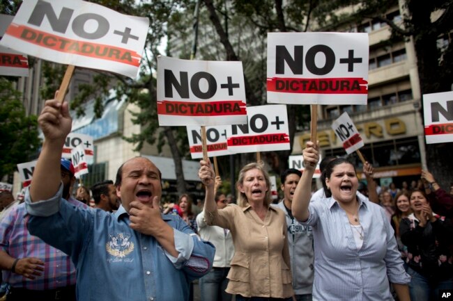 People holding signs with a message that reads in Spanish: "No more dictatorship" take part in a walkout against President Nicolas Maduro, in Caracas, Venezuela, Jan. 30, 2019.