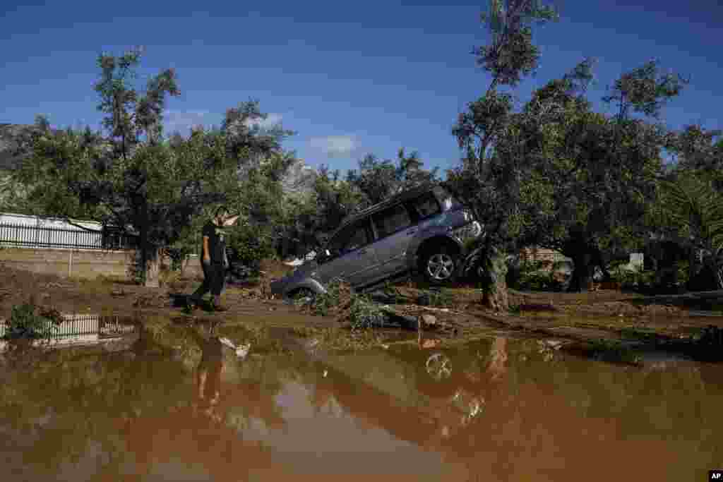 A man walks past a car moved by the force of flood water after storms in Kineta village, about 68 Kilometers (42 miles) west of Athens, Greece.