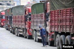 FILE - A man smokes beside trucks queuing to buy diesel at a petrol station in Luding county, Sichuan province, Oct. 23, 2011.