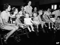 Three toddlers awaiting their turn to be inoculated with gamma globulin, blood fraction in a mass experiment to prevent paralysis from polio in this file photo dated July 2, 1952 in Houston.