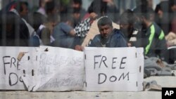 Seen through a wire fence, refugees and migrants most of them from Pakistan, hold placards during a third day of hunger strike to protest their deportation to Turkey, in the Greek island of Lesbos, April 7, 2016. 