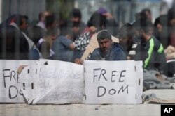FILE - Seen through a wire fence, refugees and migrants most of them from Pakistan, hold placards during a third day of hunger strike to protest their deportation to Turkey, in the Greek island of Lesbos, April 7, 2016.