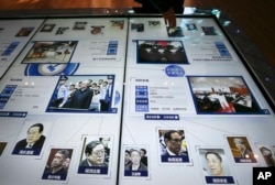 FILE - A visitor, top, looks at an electronic screen showing images and convicted corruption charges of China's fallen politicians, Bo Xilai, bottom second right, Zhou Yongkang, bottom left, and other senior officials, at the China Court Museum in Beijing.