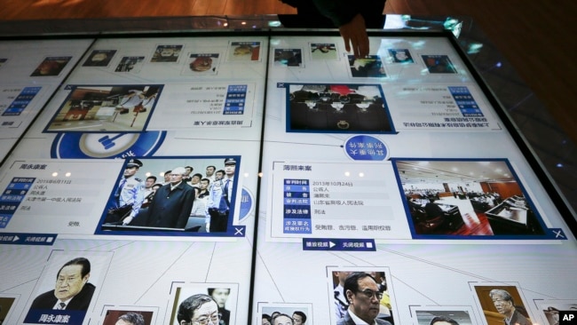FILE - A visitor, top, looks at an electronic screen displaying images and convicted corruption charges of China's fallen politicians, Bo Xilai, bottom second right, Zhou Yongkang, bottom left, and other senior officials, at the China Court Museum in Beijing.