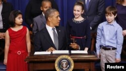 President Barack Obama talks with 11-year-old letter writer Julia Stokes (2nd R in blue dress) as he signs executive orders on gun violence during an event at the White House, January 16, 2013.