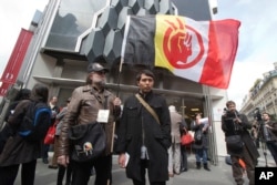 A French supporter of the Indian cause, left, holds a flag of the American Indian Movement and an American exchange student, member of Arizona's Hopi tribe, Bo Lomahquahu, right, stand outside of the Druout's auction house in Paris, April 12, 2013.