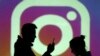 Las siluetas de los usuarios de dispositivos móviles se ven junto a una proyección en pantalla del logo de Instagram.
