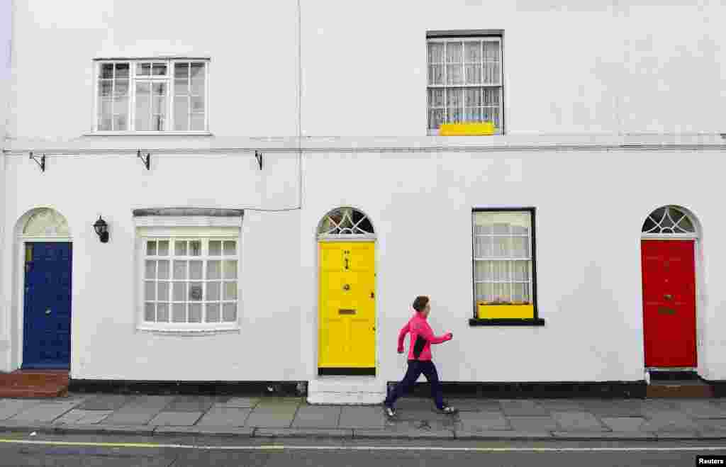 A woman takes an early morning walk past painted blue, yellow and red front doors - the colors of the current three main political parties in the U.K., Conservative, Liberal Democrat and Labour respectively - in Isleworth, west London, Britain. Britain goes to the polls in a national election on May 7.