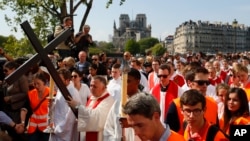 With Notre Dame cathedral in background, religious officials carry the cross during the Good Friday procession, in Paris, Apr. 19, 2019. 