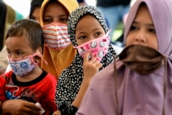 Perempuan dan anak-anak yang memakai masker menunggu pembagian makanan di tengah pandemi virus corona COVID-19 di Blang Bintang, Aceh, 6 Mei 2020. (Foto: AFP/Chaideer Mahyuddin)
