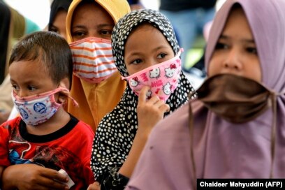 Perempuan dan anak-anak yang memakai masker menunggu pembagian makanan di tengah pandemi virus corona COVID-19 di Blang Bintang, Aceh, pada 6 Mei 2020. (Foto: AFP/Chaideer Mahyuddin)