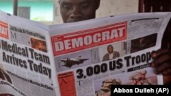 In this file photo, a man reads a news paper with headlines comment on American President Barrack Obama announcement on sending troops to fight the Ebola virus in Monrovia, Liberia, Wednesday, Sept. 17, 2014. (AP Photo/Abbas Dulleh)