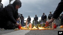 People light candles and lay flowers as police officers stand guard in front of the Government building in Skopje, Macedonia, May 11, 2015.